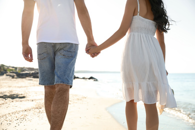 Photo of Young couple walking on beach near sea, closeup. Honeymoon trip