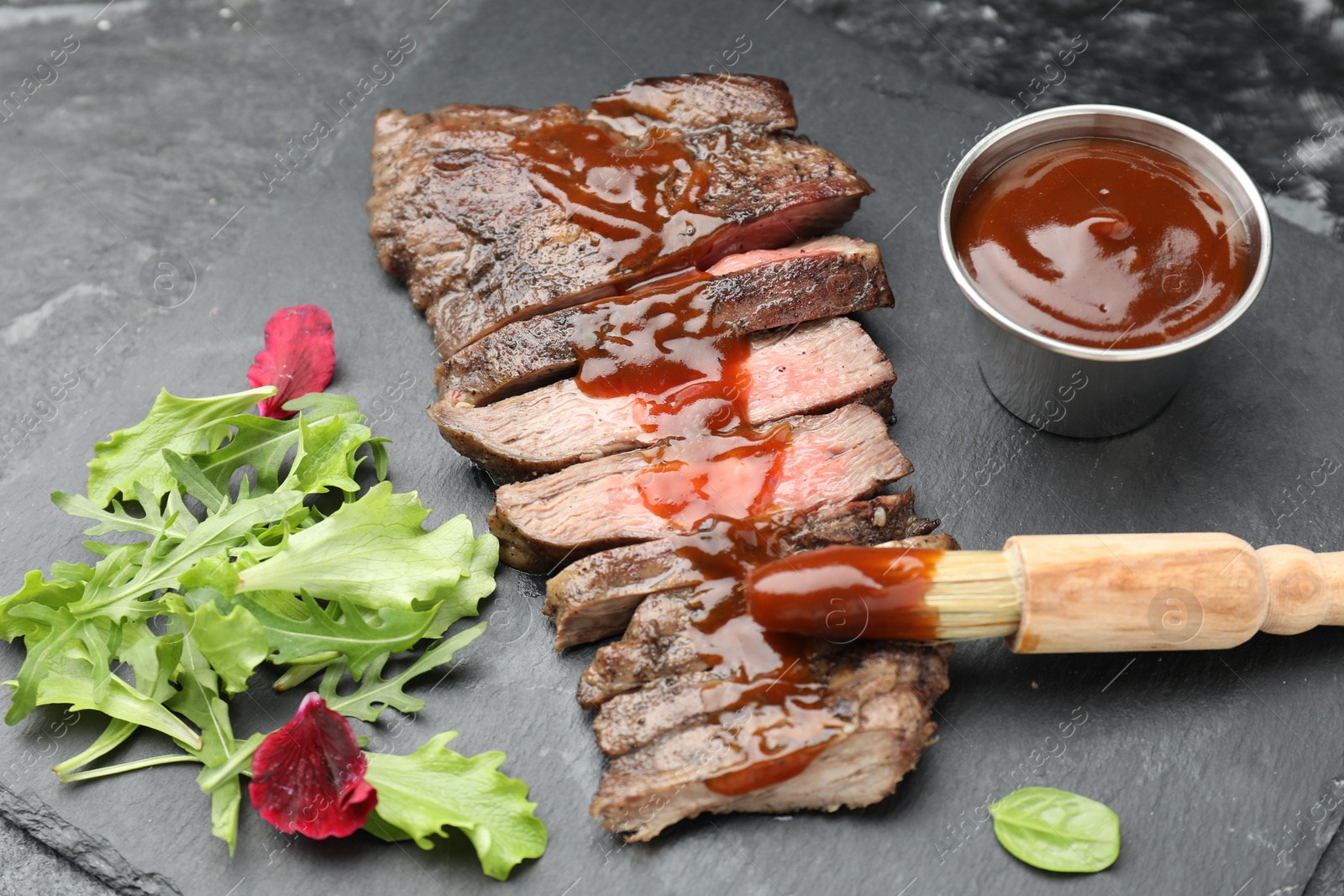 Photo of Pieces of delicious roasted beef meat with sauce and greens on black table, closeup