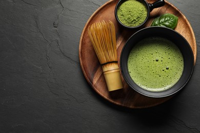 Photo of Cup of fresh matcha tea, bamboo whisk and green powder on black table, top view. Space for text
