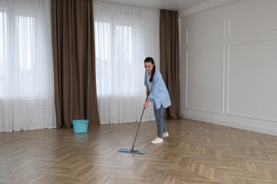 Photo of Young woman cleaning floor with mop in empty room