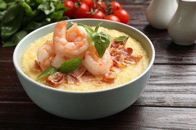 Photo of Fresh tasty shrimps, bacon, grits and basil in bowl on wooden table, closeup