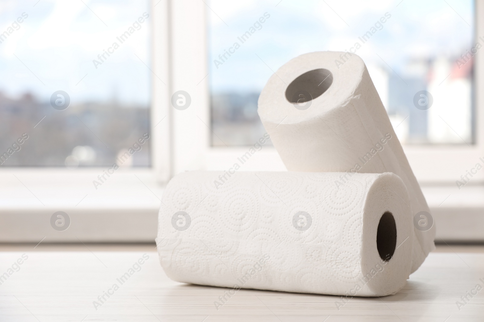 Photo of Rolls of paper towels on white wooden table indoors. Space for text