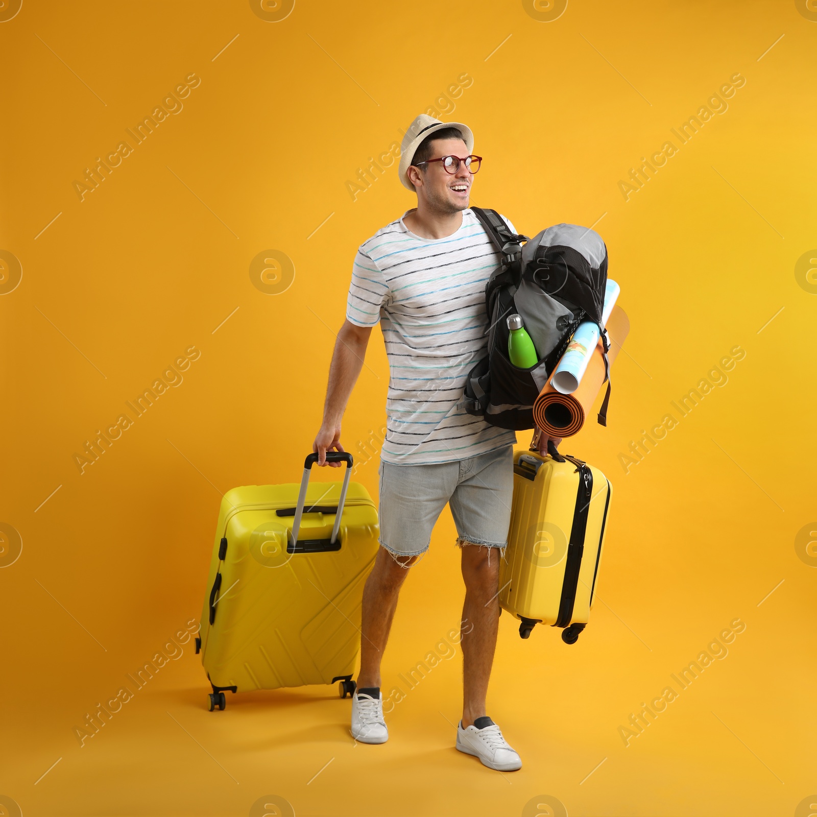 Photo of Male tourist with travel backpack and suitcases on yellow background