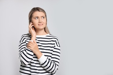 Young woman suffering from ear pain on light grey background. Space for text