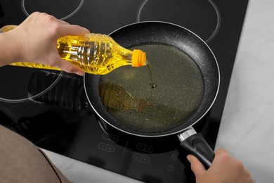 Photo of Woman pouring cooking oil from bottle into frying pan on stove, above view