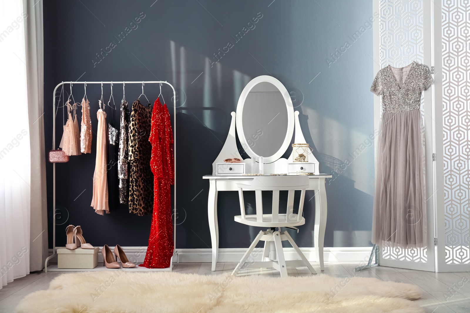 Photo of Rack with collection of beautiful festive clothes and dressing table in stylish room interior