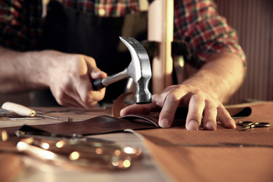 Photo of Man working with piece of leather at table, closeup