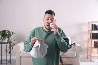 Photo of Man with vacuum cleaner bag suffering from dust allergy at home