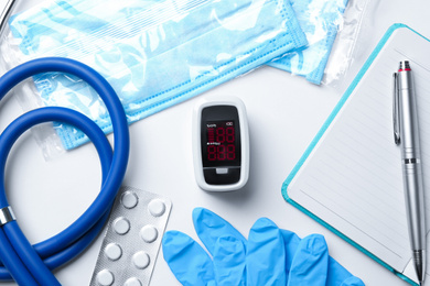 Flat lay composition with modern fingertip pulse oximeter and medical items on white background