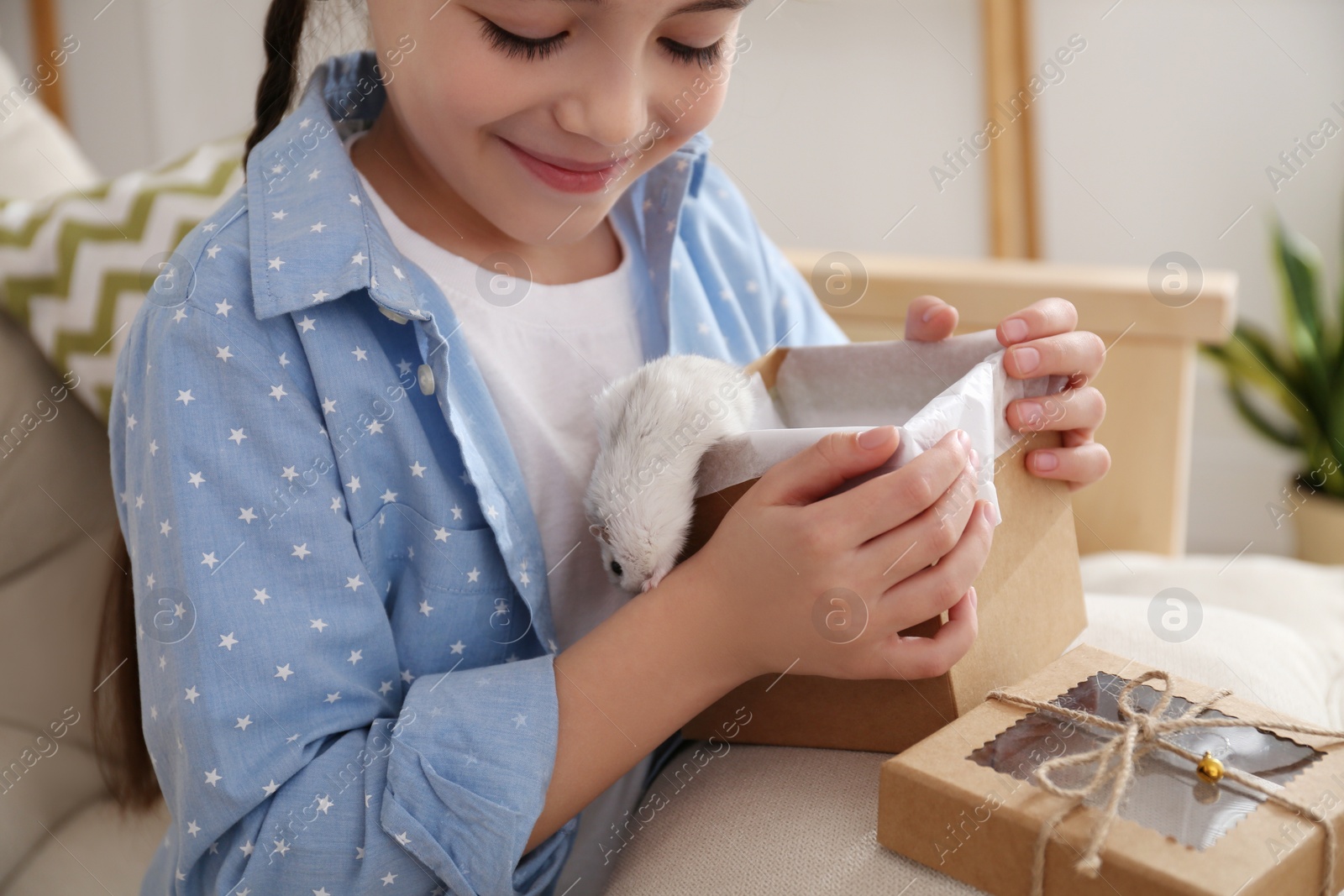 Photo of Happy little girl holding gift box with cute hamster at home