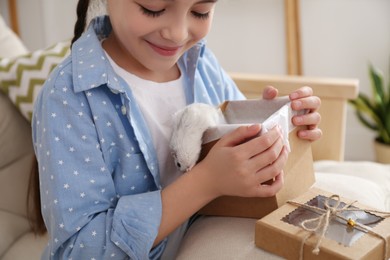 Photo of Happy little girl holding gift box with cute hamster at home