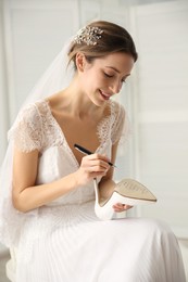 Photo of Young bride writing her single friends names on shoe indoors. Wedding superstition