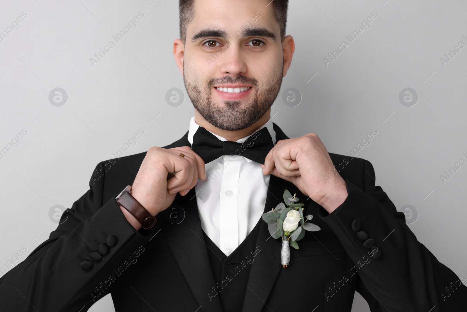 Photo of Handsome young groom with boutonniere on light grey background. Wedding accessory