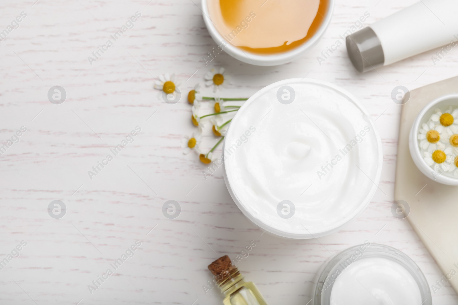 Photo of Body cream and other cosmetics, honey with camomile on white wooden table, flat lay. Space for text