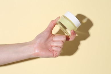 Woman holding jar of cream on yellow background, closeup