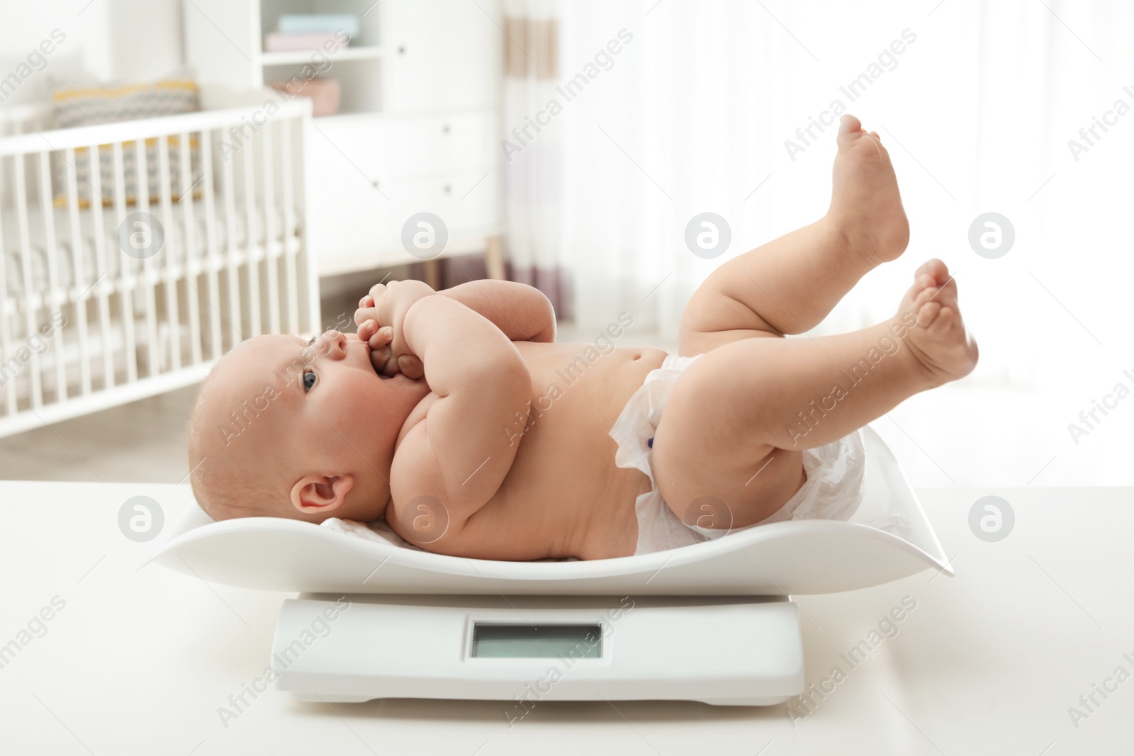 Photo of Cute little baby lying on scales in light room