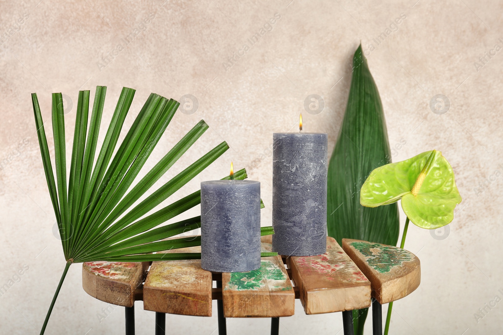 Photo of Creative composition with candles and tropical plants on color background