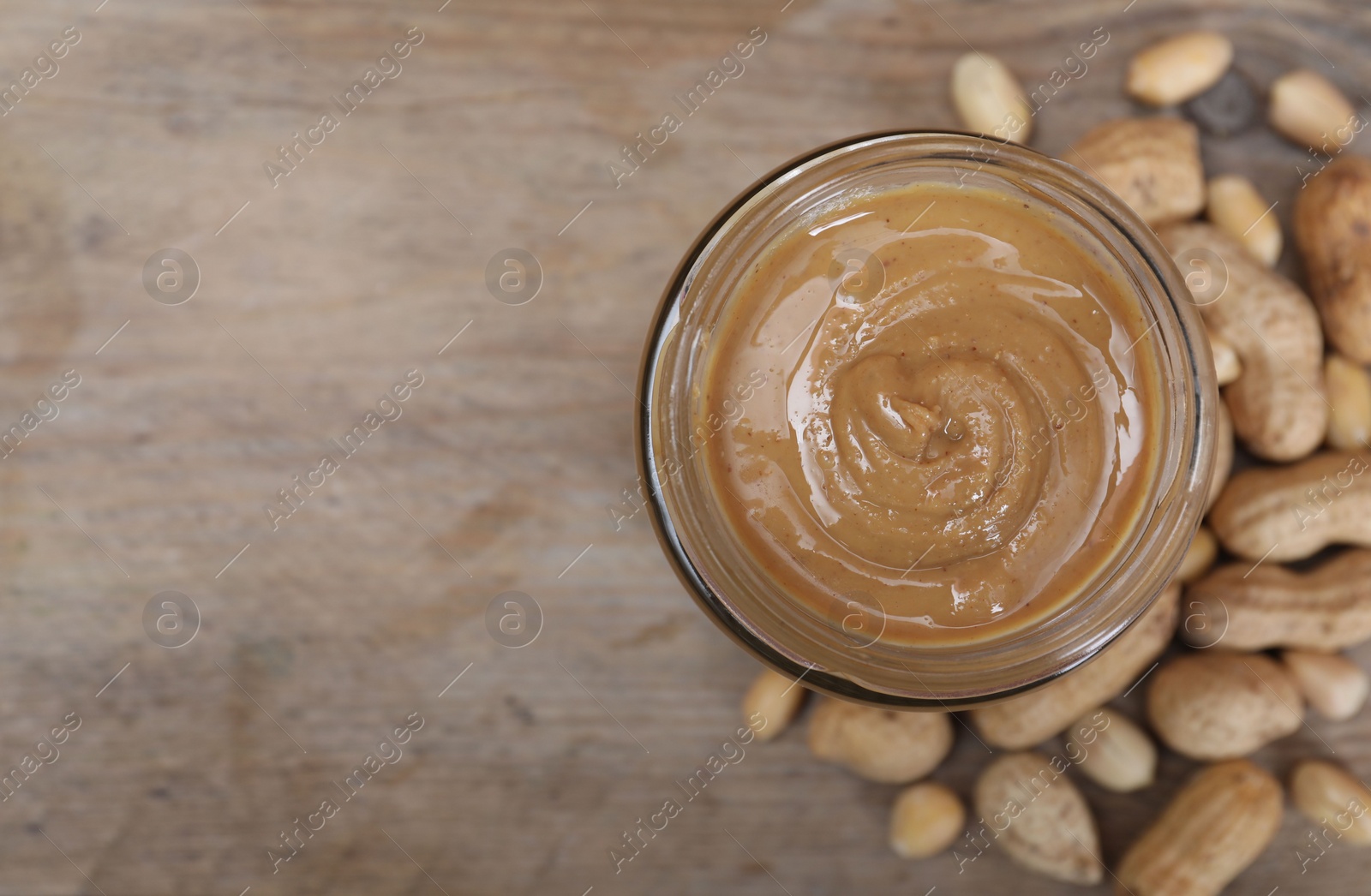 Photo of Tasty peanut nut paste in jar on wooden table, top view. Space for text