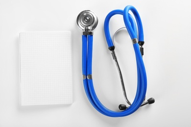 Photo of Stethoscope and blank notebook on light background. Heart attack concept