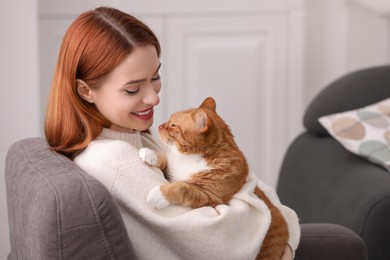 Photo of Happy woman with her cute cat in armchair at home