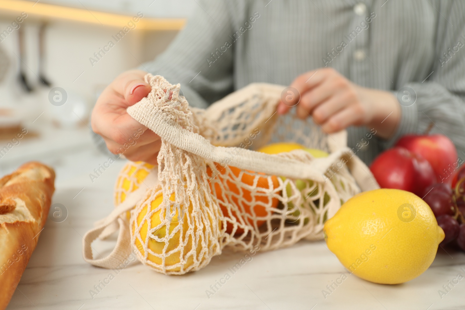 Photo of Woman with string bag of fresh fruits at light marble table, closeup