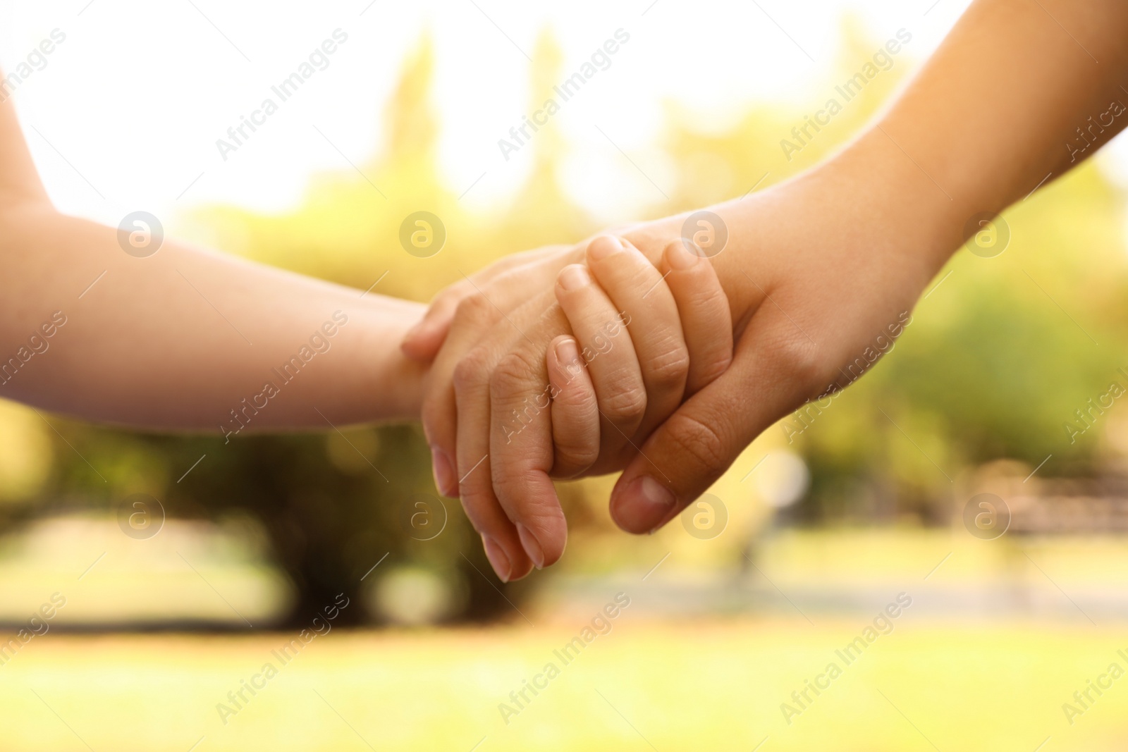 Photo of Little child and mother holding hands outdoors, closeup. Family weekend