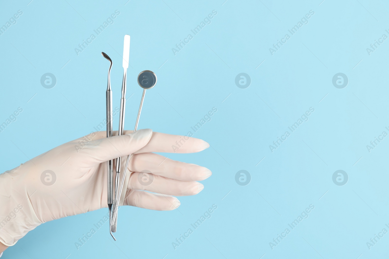 Photo of Dentist holding set of tools on light blue background, closeup. Space for text