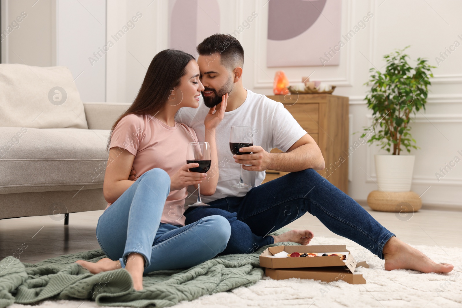 Photo of Affectionate young couple eating pizza and drinking wine at home