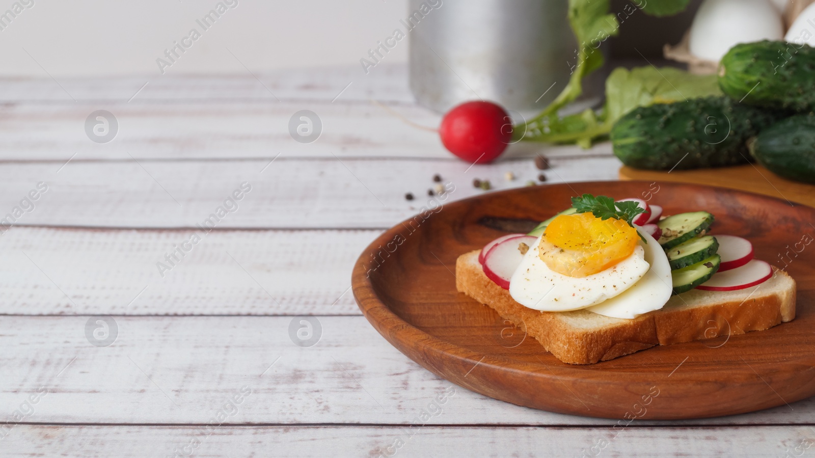 Photo of Tasty sandwich with boiled egg, radish, cucumber and ingredients on white wooden table, space for text