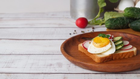 Tasty sandwich with boiled egg, radish, cucumber and ingredients on white wooden table, space for text