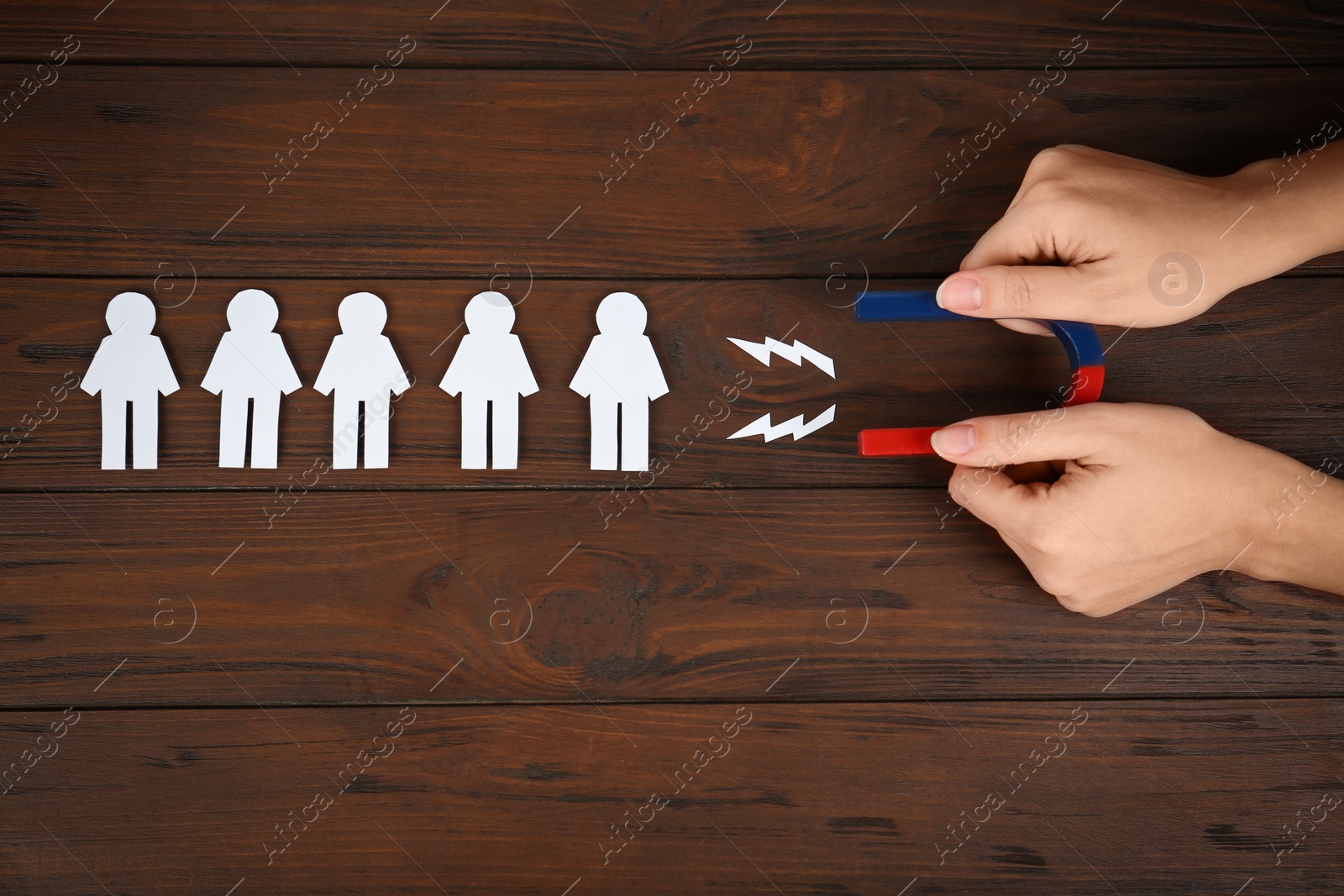 Photo of Woman attracting paper people with magnet at wooden table, top view