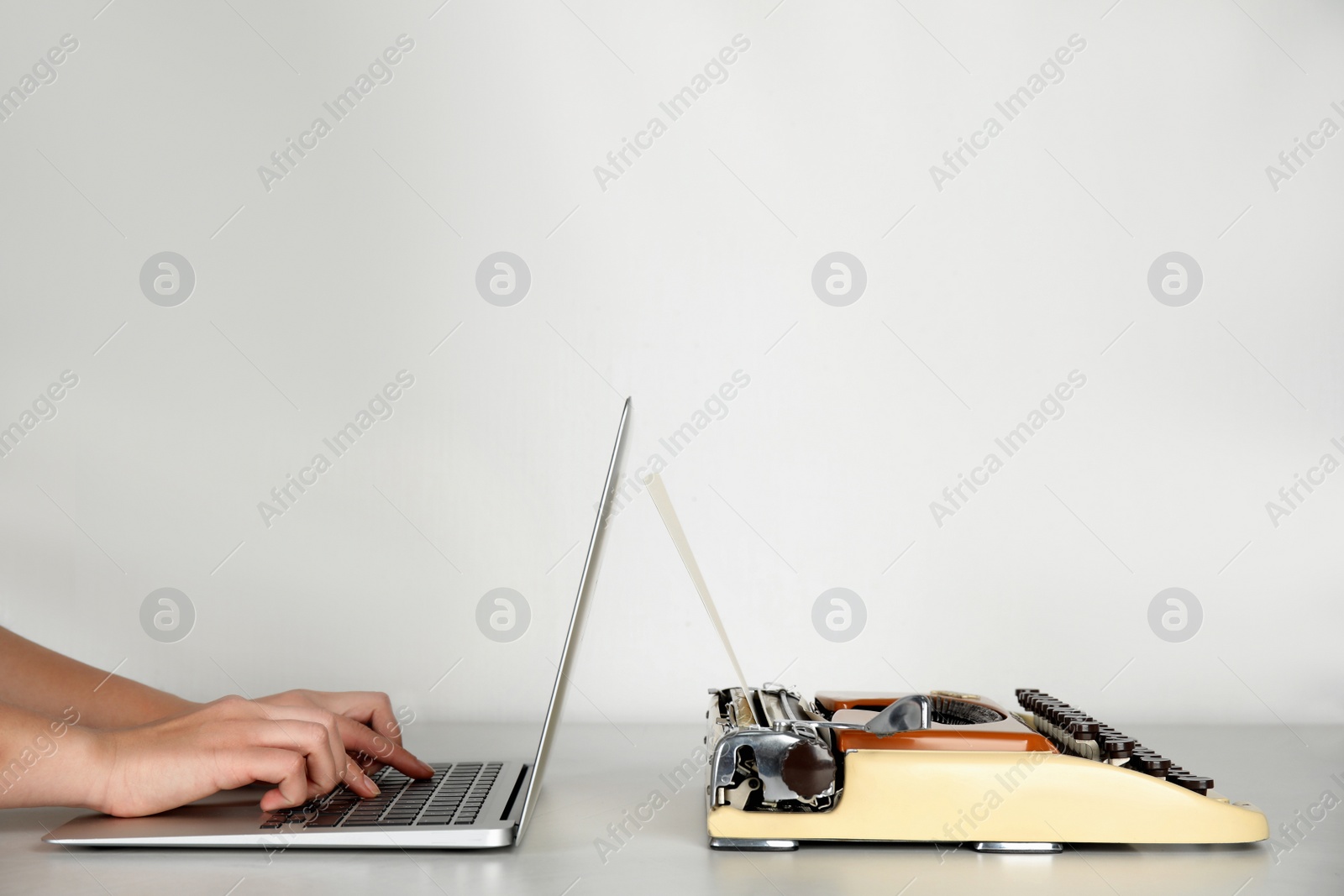 Photo of Woman using laptop near old typewriter at table against light background, closeup with space for text. Concept of technology progress