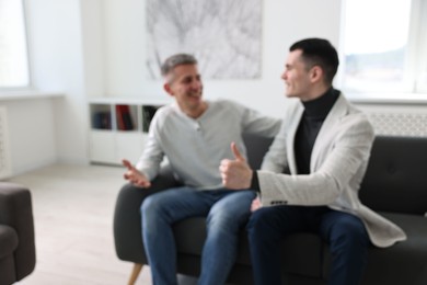 Photo of Blurred view of happy men talking while sitting on sofa at home