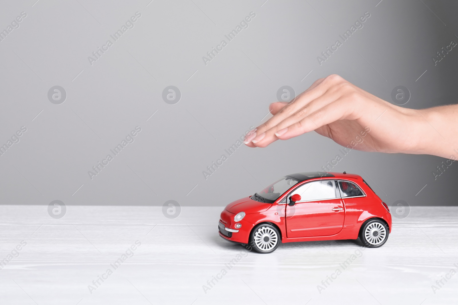 Photo of Insurance agent covering toy car on table, closeup. Space for text