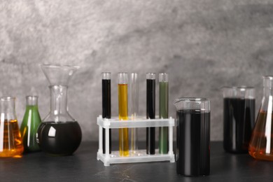 Photo of Beaker, flasks and test tubes with different types of oil on grey textured table, closeup