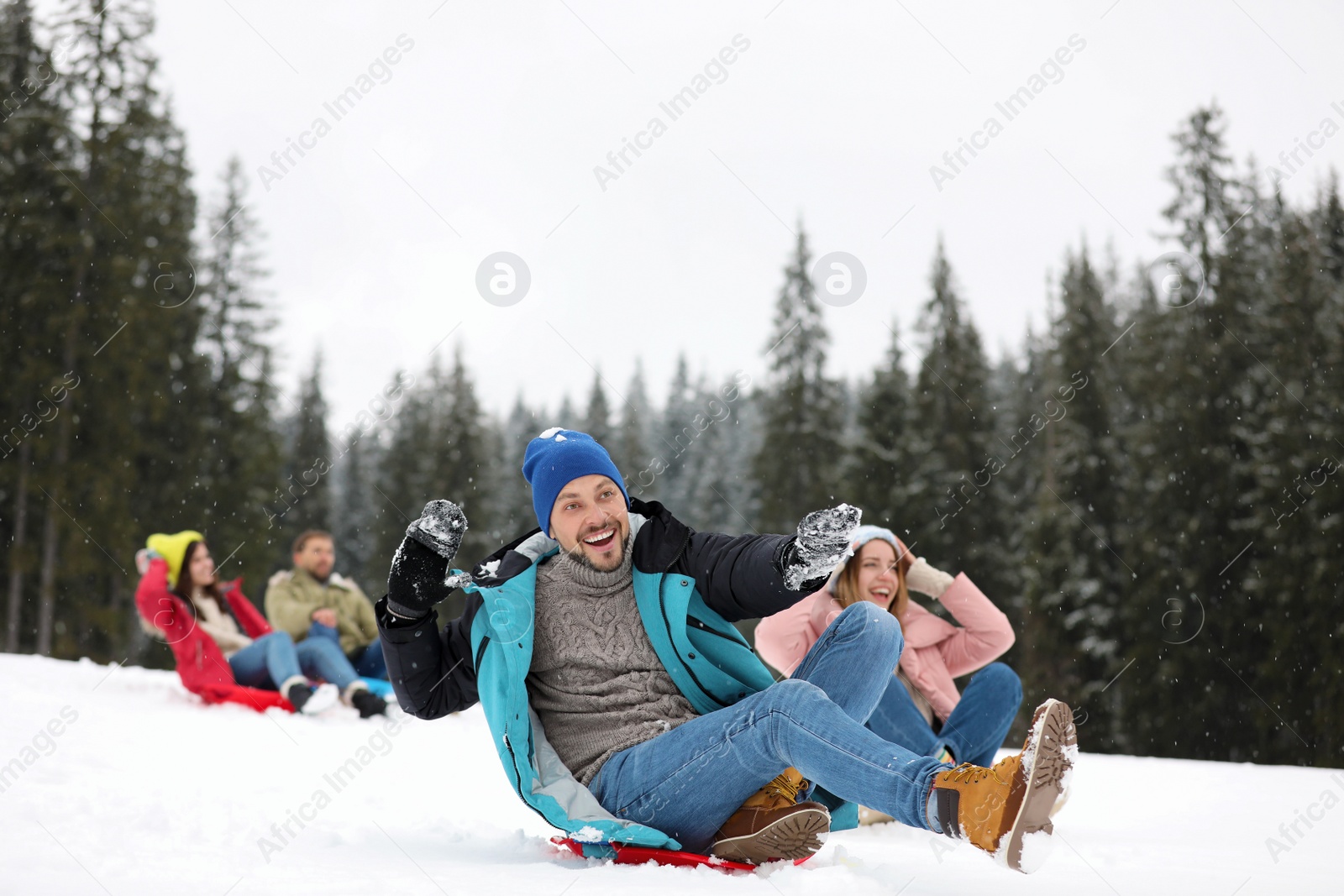 Photo of Happy friends sliding on sleds outdoors. Winter vacation