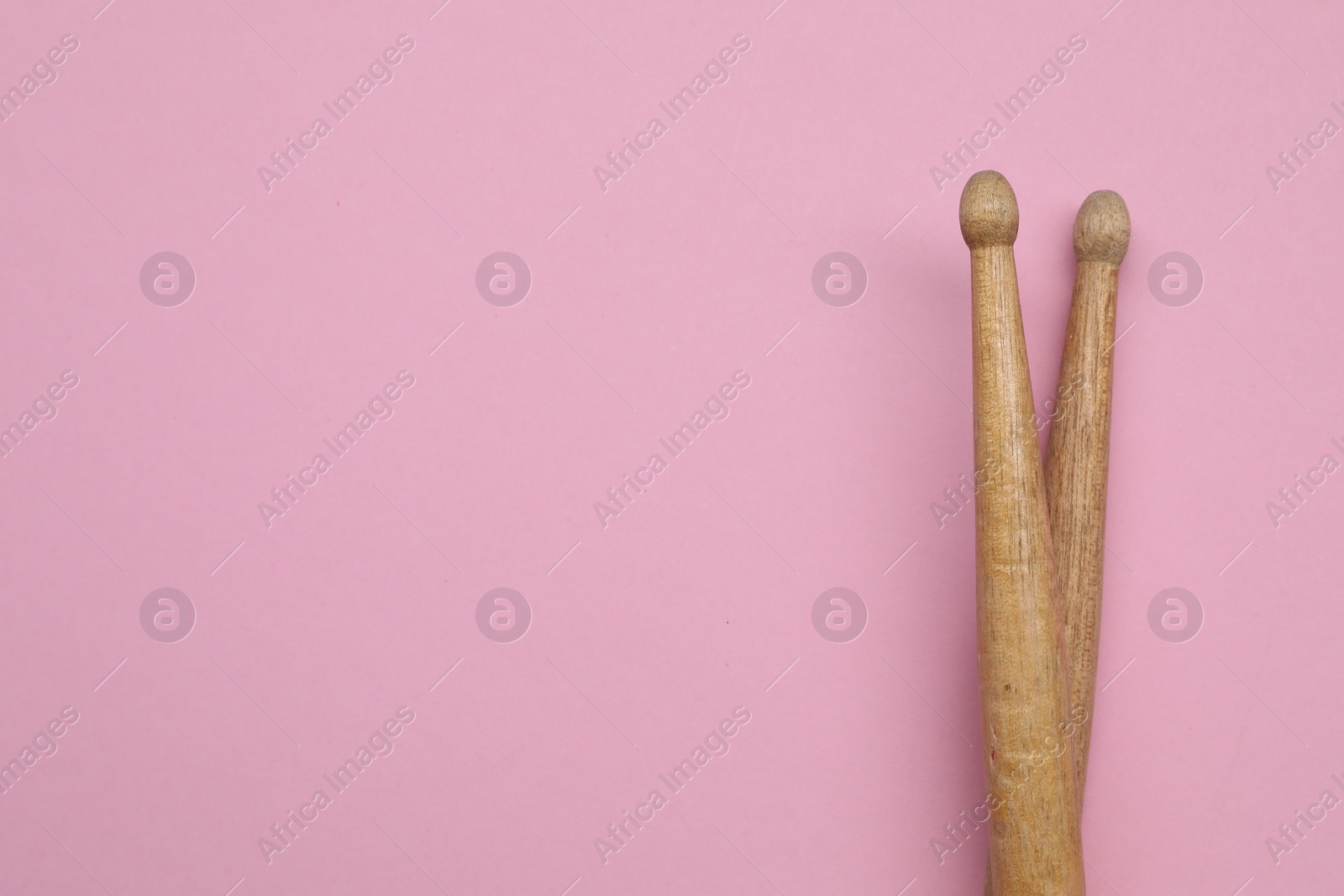 Photo of Two wooden drum sticks on pink background, top view. Space for text