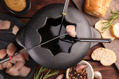 Fondue pot, forks, pieces of raw meat, bread and spices on wooden table, flat lay