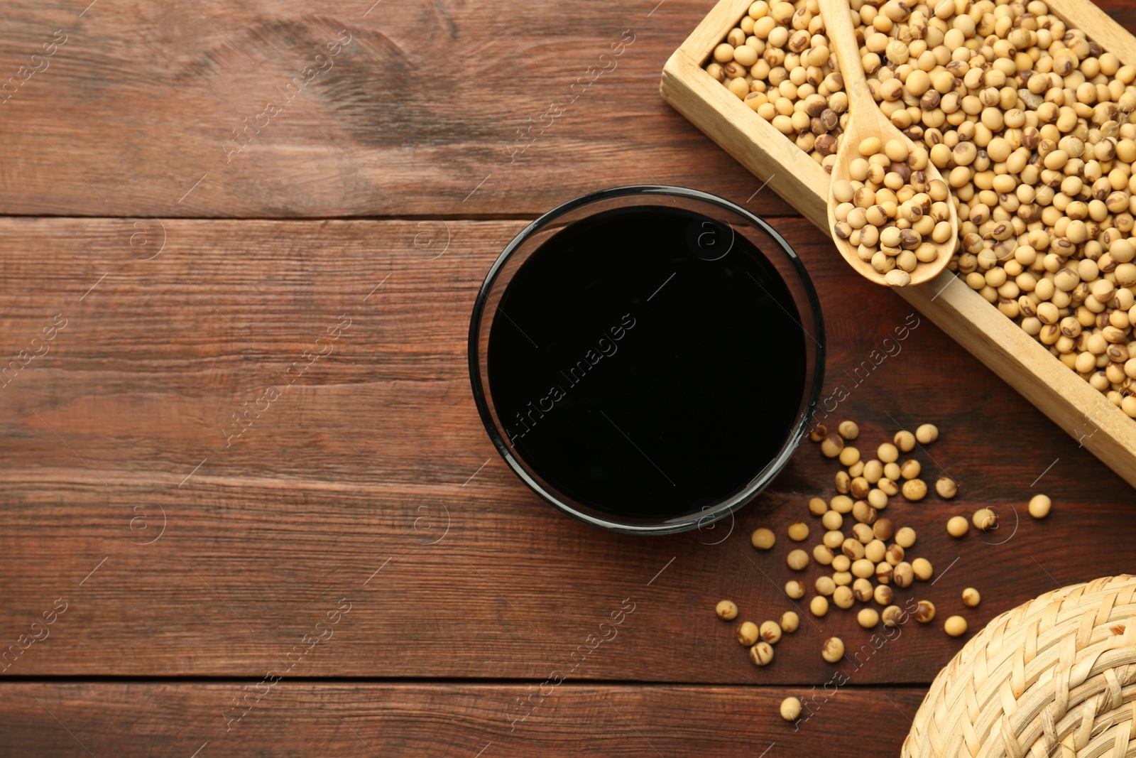 Photo of Soy sauce in bowl and soybeans on wooden table, flat lay. Space for text