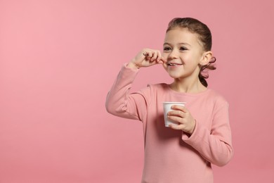 Girl eating tasty yogurt on pink background, space for text