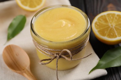 Delicious lemon curd in bowl, fresh citrus fruit and spoon on wooden table, closeup