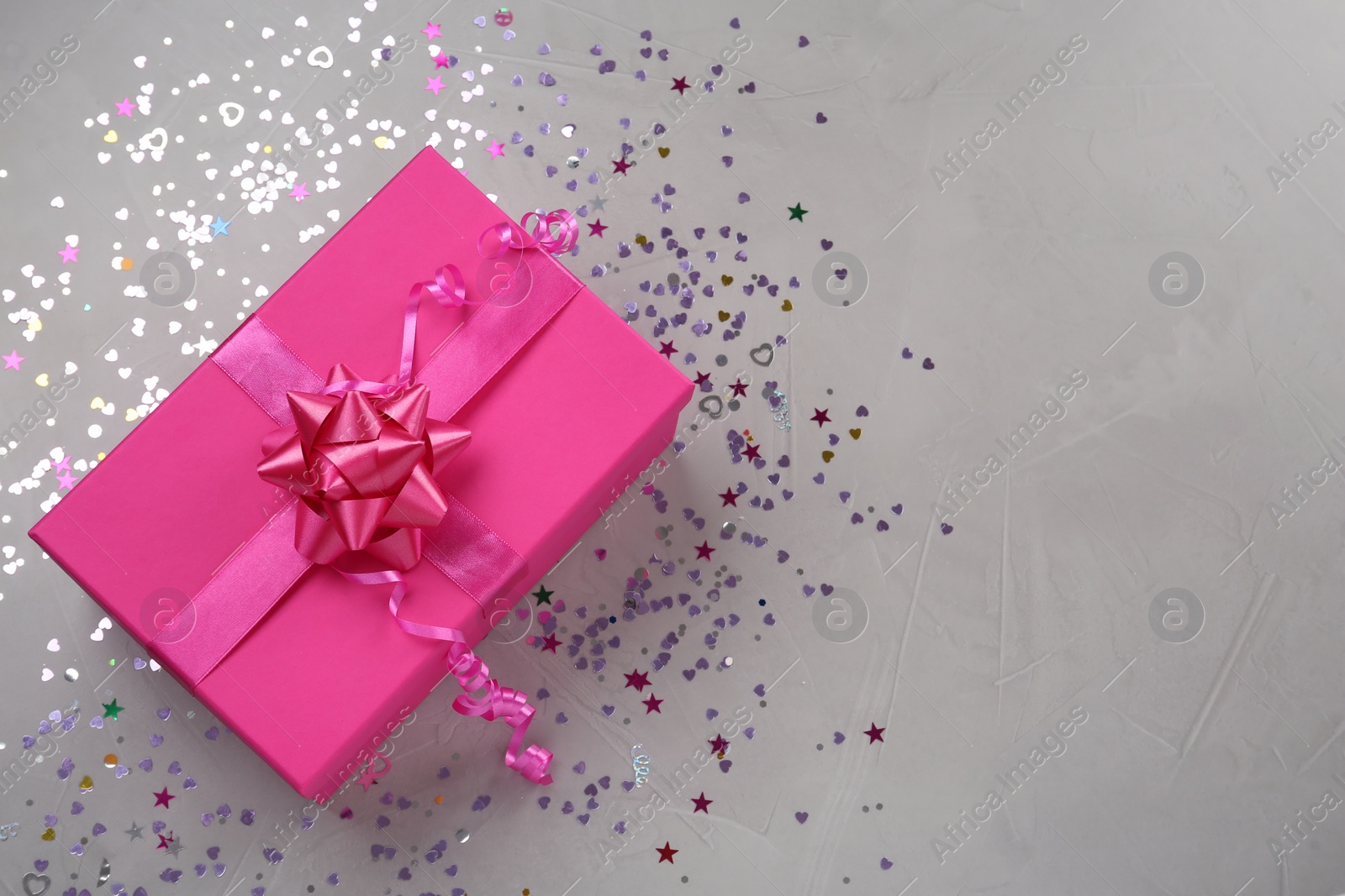 Photo of Pink gift box and shiny confetti on grey background, top view. Space for text