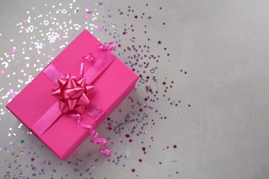 Photo of Pink gift box and shiny confetti on grey background, top view. Space for text