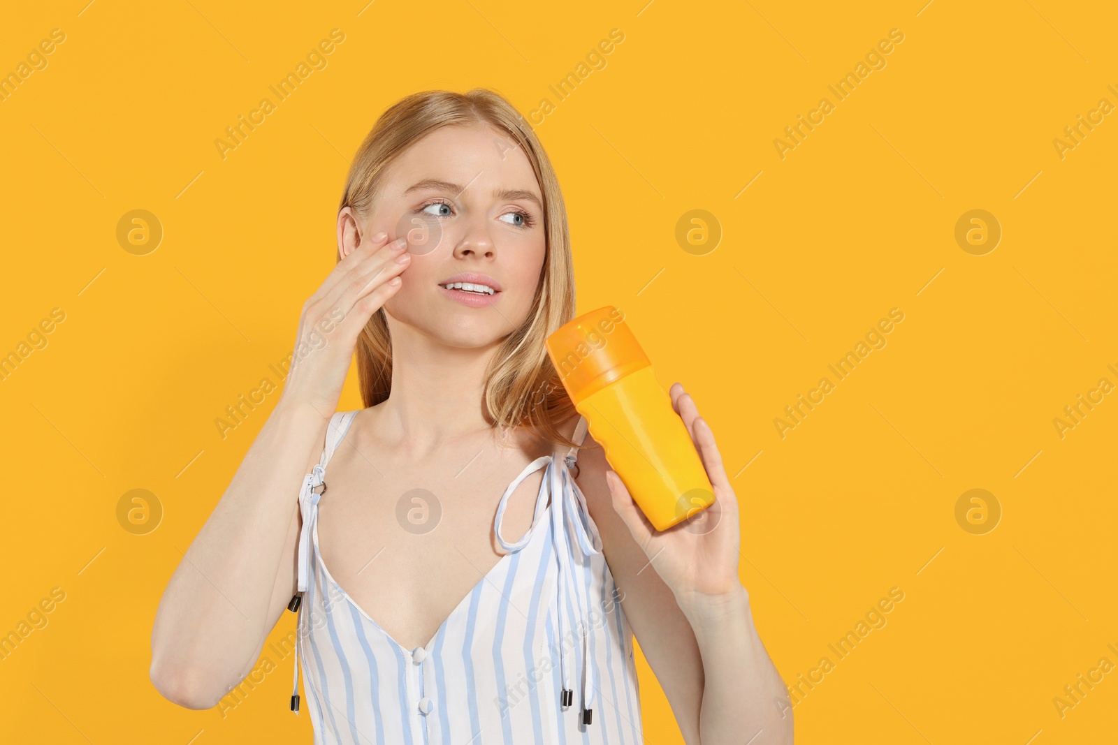 Photo of Beautiful young woman holding sun protection cream on orange background, space for text