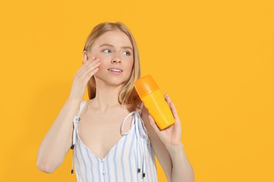 Beautiful young woman holding sun protection cream on orange background, space for text