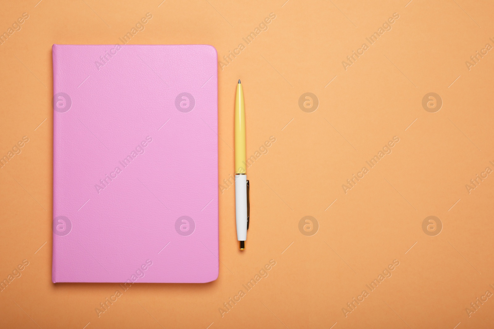 Photo of Closed pink notebook and pen on pale orange background, flat lay. Space for text