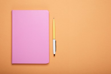 Photo of Closed pink notebook and pen on pale orange background, flat lay. Space for text