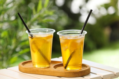 Plastic cups of tasty iced tea with lemon on white wooden table against blurred background