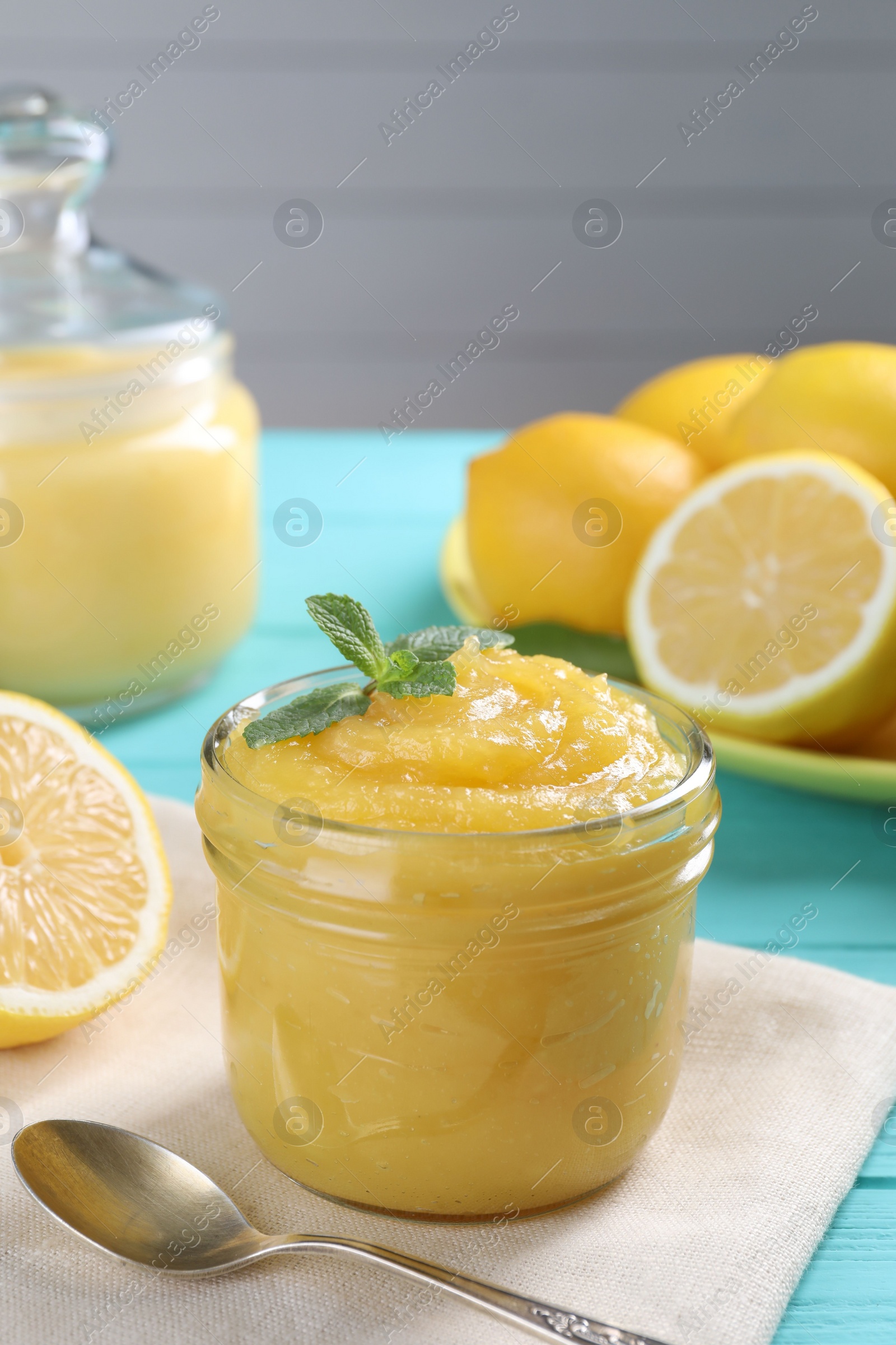 Photo of Delicious lemon curd in glass jar, fresh citrus fruits, mint and spoon on light blue wooden table