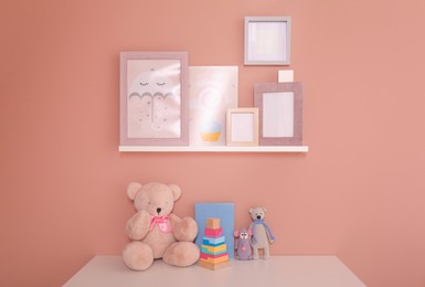 Photo of Book with toys on table and pictures near beige wall. Interior design